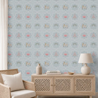 A modern bohemian living room or entryway featuring a powder blue Vraj Kamal Pichwai wallpaper patterned with cows and pink lotuses, styled with a light wood cane chair, a minimalist wooden console cabinet, and neutral decor.
