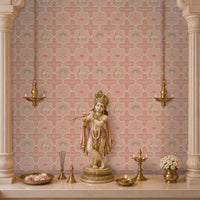 A beautifully styled Indian mandir backdrop or pooja room altar framed by architectural pillars, featuring a pink Vraj Kamal Pichwai wallpaper with repeating cow and lotus motifs behind a standing Lord Krishna idol and brass lamps.
