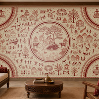 Warli Divine Harmony - Warm Ivory seamless wallpaper featuring intricate Warli tribal art with a central Radha Krishna motif, surrounded by village scenes, trees, huts, dancers, animals, and geometric borders in terracotta red on a warm ivory background. Displayed in a traditional Indian living room with carved wooden furniture and ethnic décor.