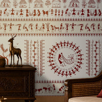 A traditional Indian living room titled “Warli Folk Tales – Vintage Red on White.” The focal wall is painted white and adorned with intricate earthy red Warli tribal art depicting village life, including dancing figures, farming scenes, huts, animals, and trees arranged in horizontal bands. Wooden furniture with ornate carvings, brass decorative items, and a patterned rug enhance the cultural richness, while soft lighting creates a warm and inviting atmosphere. The design blends indigenous artistry.