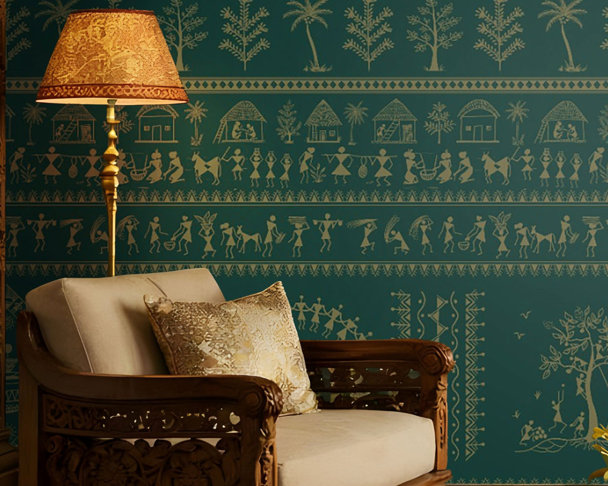 A traditional Indian living room titled “Warli Folk Tales – Vintage Teal Green.” The focal wall is painted in a deep teal shade and adorned with golden Warli tribal art depicting village life, dancing figures, huts, and trees in horizontal bands. Two intricately carved wooden armchairs with cushions flank a central coffee table decorated with brass items and a bowl of white flowers. Hanging brass pendant lamps and a golden table lamp cast a warm glow.