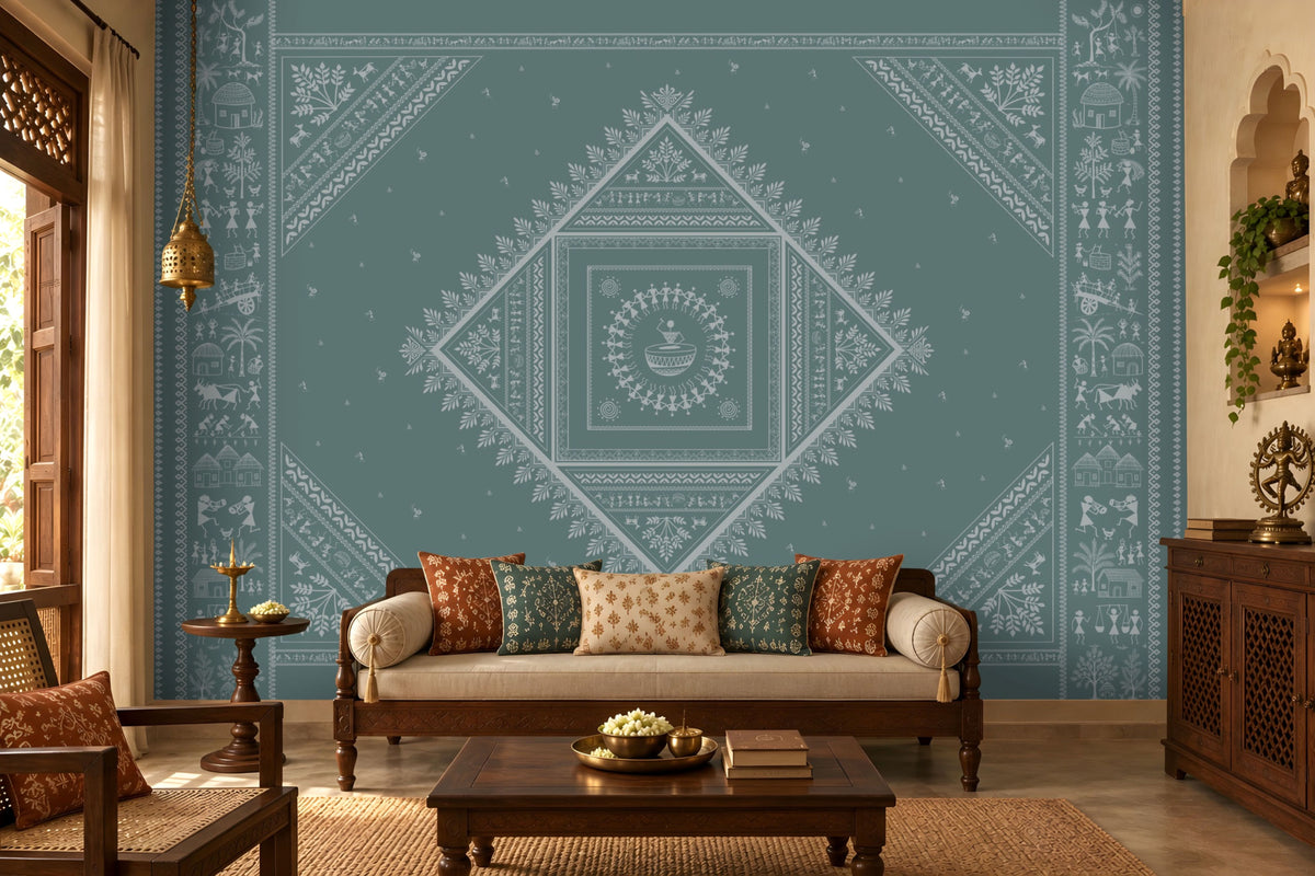A styled living room featuring a large teal wall mural with intricate white Indian folk art patterns, including a central diamond mandala. The room is furnished with a cream-colored sofa decorated with patterned cushions, a dark wood coffee table, and traditional wooden furniture.