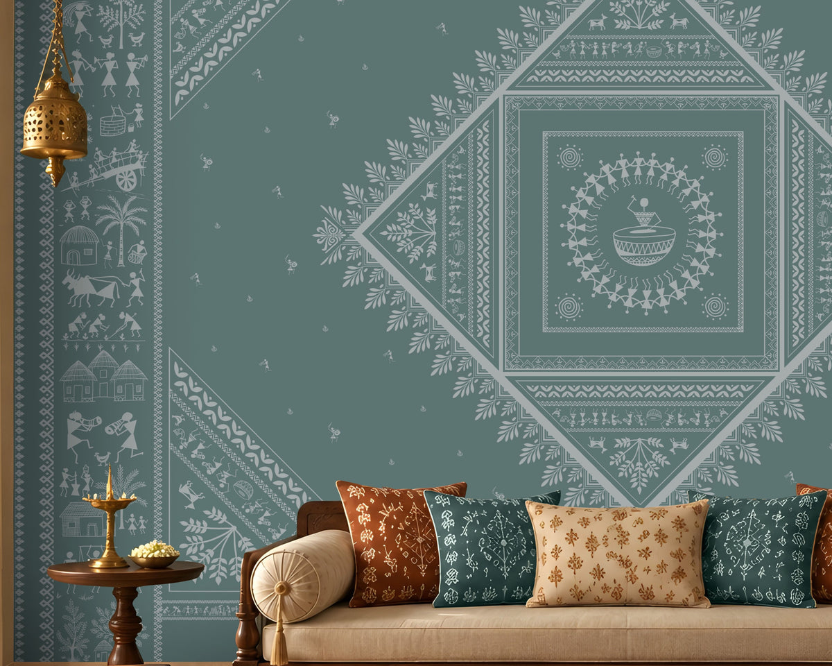 A styled living room featuring a large teal wall mural with intricate white Indian folk art patterns, including a central diamond mandala. The room is furnished with a cream-colored sofa decorated with patterned cushions, a dark wood coffee table, and traditional wooden furniture.