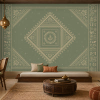 A large decorative wall mural with a symmetrical mandala and geometric tribal pattern in muted sage green and cream, installed in a styled living room with a daybed, wooden furniture, and warm ambient lighting.