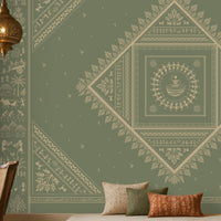 A large decorative wall mural with a symmetrical mandala and geometric tribal pattern in muted sage green and cream, installed in a styled living room with a daybed, wooden furniture, and warm ambient lighting.