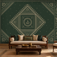 A styled living room featuring a large dark green wall mural with intricate cream-colored traditional geometric and floral patterns. In front of the wall is a wooden sofa with cream cushions, a dark wood coffee table, and a matching armchair.