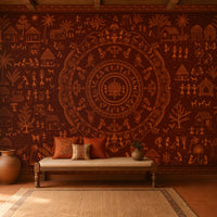 A large wall mural featuring intricate Indian folk art and a central mandala design in warm terracotta and brown tones, displayed in a styled room with a wooden bench, cushions, and a rug.