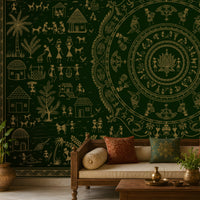 A large dark green wall tapestry with intricate beige folk art illustrations of houses, trees, and circular mandala motifs, displayed in a styled living room behind a wooden sofa.