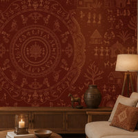 A styled living room featuring a deep terracotta red wallpaper with an intricate tan and brown Indian-style mandala and folk art pattern. The room includes a wooden console table, a lit floor lamp, a beige sofa with a matching patterned throw pillow, and a decorative ceramic pot.