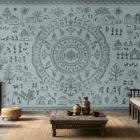 A large wall mural featuring a detailed blue-gray circular mandala and surrounding folk-art style illustrations of houses, people, and plants, shown in a styled living room with wooden furniture and woven decor.