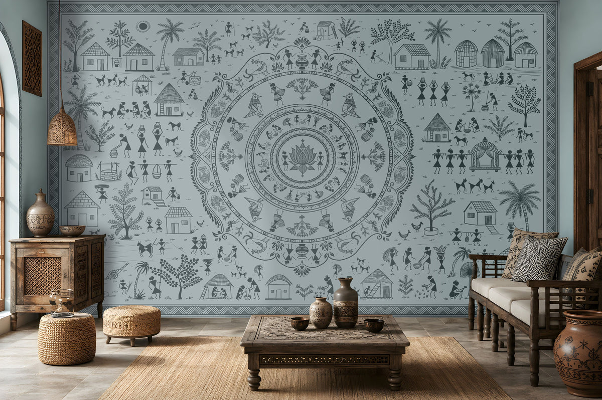 A large wall mural featuring a detailed blue-gray circular mandala and surrounding folk-art style illustrations of houses, people, and plants, shown in a styled living room with wooden furniture and woven decor.