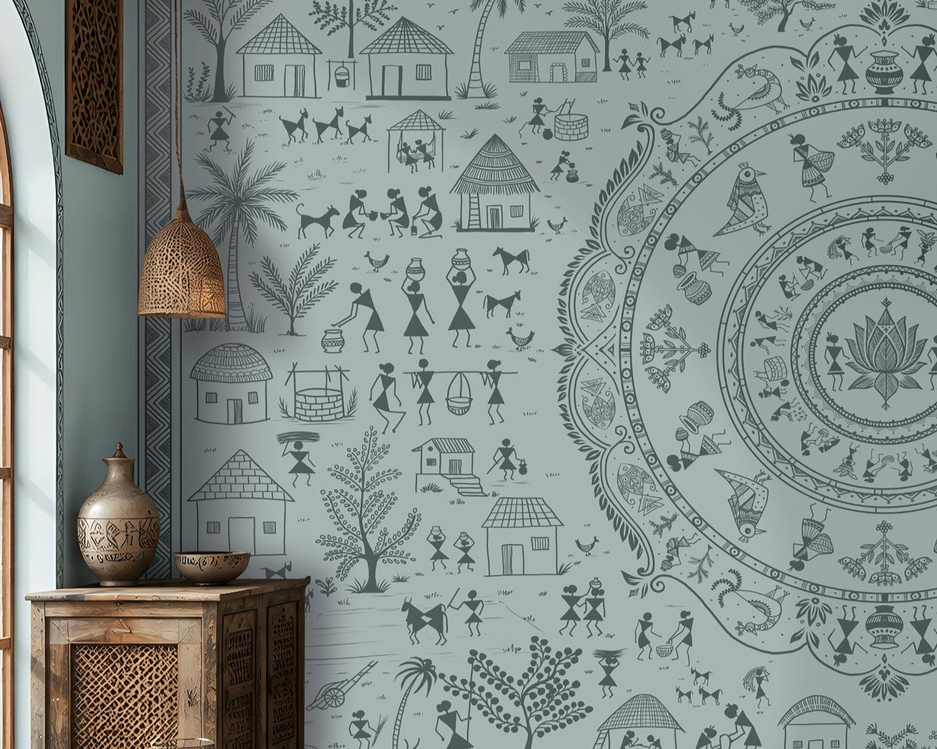 A large wall mural featuring a detailed blue-gray circular mandala and surrounding folk-art style illustrations of houses, people, and plants, shown in a styled living room with wooden furniture and woven decor.