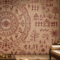A styled interior room featuring a large wall mural or wallpaper with a beige background and dark reddish-brown traditional folk art illustrations, including a central mandala-like circular motif, figures, trees, huts, and animals. Part of a cream sofa, a side table, and a lamp are visible in the room.