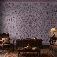 A styled traditional living room featuring a large lavender wall mural with a detailed central mandala and surrounding folk-art illustrations in muted red-brown. The room is furnished with dark wood furniture, patterned cushions, a brass table lamp, and a patterned area rug.