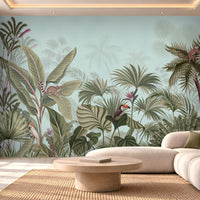 Illustrated tropical jungle wallpaper featuring dense, muted green and sage foliage set against a soft light blue backdrop. The detailed scene showcases a variety of exotic plants, including large banana leaves and fan palms, interspersed with wildlife like, a ring-tailed lemur, a toucan, and a small monkey climbing a palm tree.