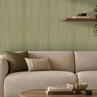 Modern living room with a soft green textured accent wall, cream upholstered sofa and armchair, warm floor lamp, floating wooden shelves with books and plants, and a round wooden coffee table on a neutral area rug. Natural light enters through a large window with beige curtains, creating a calm, contemporary interior.
