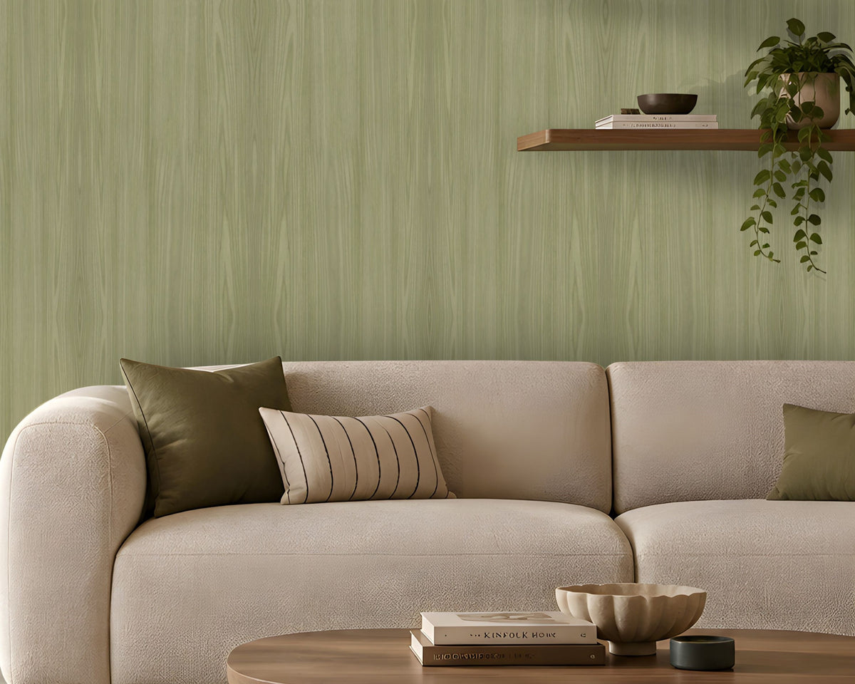 Modern living room with a soft green textured accent wall, cream upholstered sofa and armchair, warm floor lamp, floating wooden shelves with books and plants, and a round wooden coffee table on a neutral area rug. Natural light enters through a large window with beige curtains, creating a calm, contemporary interior.