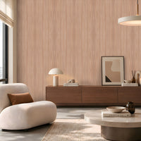 Contemporary living room featuring a light wood-grain accent wall, a curved cream lounge chair with a brown cushion, a dark wooden sideboard styled with books, a table lamp and decorative accessories, and a round stone coffee table. Soft daylight streams through a large window, creating a warm, minimalist atmosphere with neutral tones and natural textures.