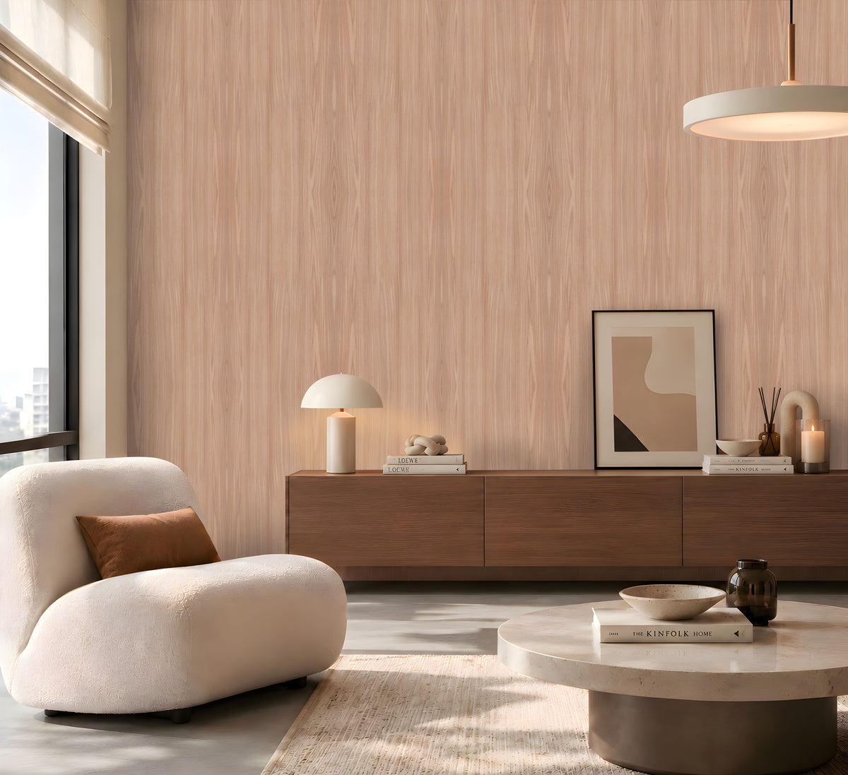 Contemporary living room featuring a light wood-grain accent wall, a curved cream lounge chair with a brown cushion, a dark wooden sideboard styled with books, a table lamp and decorative accessories, and a round stone coffee table. Soft daylight streams through a large window, creating a warm, minimalist atmosphere with neutral tones and natural textures.