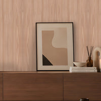 Contemporary living room featuring a light wood-grain accent wall, a curved cream lounge chair with a brown cushion, a dark wooden sideboard styled with books, a table lamp and decorative accessories, and a round stone coffee table. Soft daylight streams through a large window, creating a warm, minimalist atmosphere with neutral tones and natural textures.
