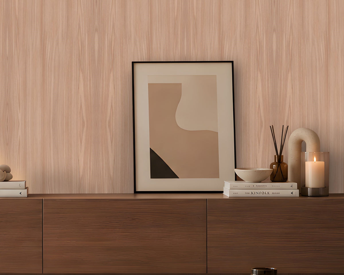 Contemporary living room featuring a light wood-grain accent wall, a curved cream lounge chair with a brown cushion, a dark wooden sideboard styled with books, a table lamp and decorative accessories, and a round stone coffee table. Soft daylight streams through a large window, creating a warm, minimalist atmosphere with neutral tones and natural textures.
