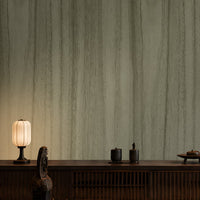 Wood Seamless Wallpaper - Moss Green displayed in a sophisticated Japandi-inspired living space. The wallpaper features a muted moss green tone with subtle vertical wood grain textures, creating a seamless natural look. Paired with dark wooden furniture, soft ambient lighting, neutral floor cushions, and elegant décor accents, the wallpaper adds depth, warmth, and a calming organic aesthetic to the interior.