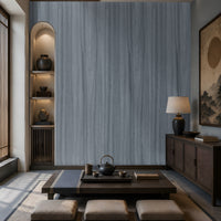 Wood Seamless Wallpaper - Stone Blue featured in a Japandi-inspired living space. The wallpaper showcases a seamless vertical wood grain texture in soft ash grey tones, creating a sophisticated and calming backdrop. Paired with dark wood furniture, built-in illuminated shelving, neutral floor cushions, and warm ambient lighting, the design adds depth, elegance, and a contemporary natural aesthetic to the interior.