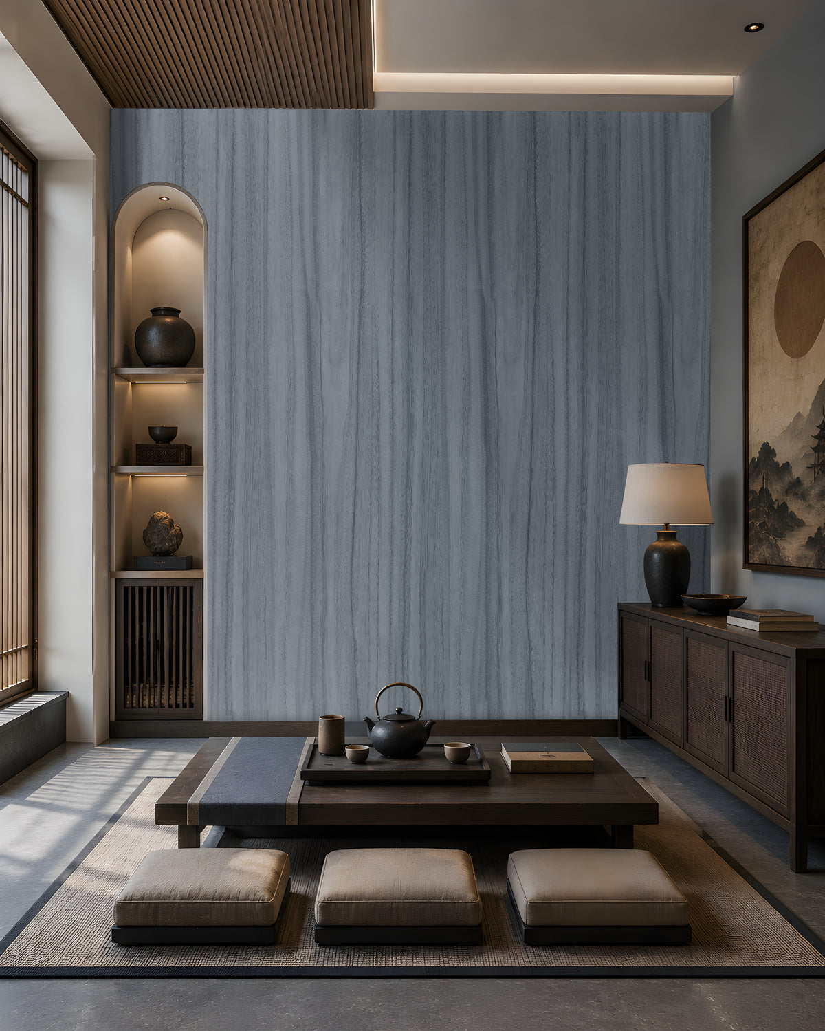 Wood Seamless Wallpaper - Stone Blue featured in a Japandi-inspired living space. The wallpaper showcases a seamless vertical wood grain texture in soft ash grey tones, creating a sophisticated and calming backdrop. Paired with dark wood furniture, built-in illuminated shelving, neutral floor cushions, and warm ambient lighting, the design adds depth, elegance, and a contemporary natural aesthetic to the interior.