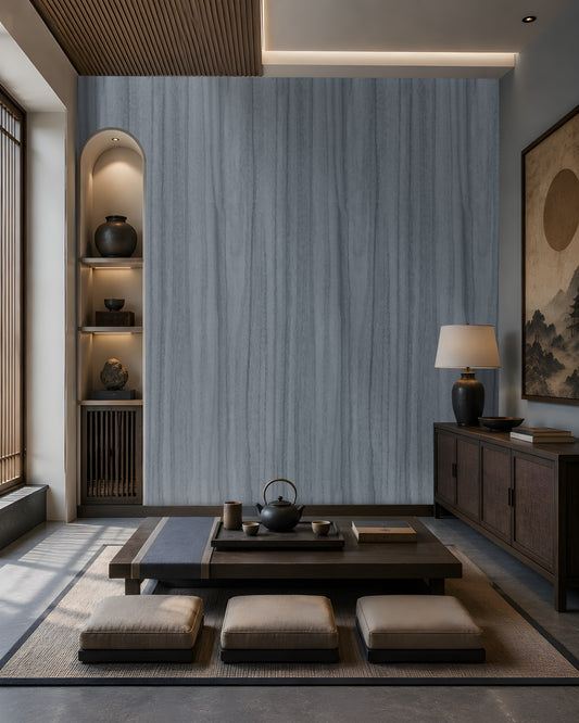 Wood Seamless Wallpaper - Stone Blue featured in a Japandi-inspired living space. The wallpaper showcases a seamless vertical wood grain texture in soft ash grey tones, creating a sophisticated and calming backdrop. Paired with dark wood furniture, built-in illuminated shelving, neutral floor cushions, and warm ambient lighting, the design adds depth, elegance, and a contemporary natural aesthetic to the interior.