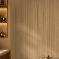 Wood Seamless Wallpaper - Wheat Cream displayed in a cozy contemporary interior. The wallpaper features a warm wheat cream tone with subtle vertical wood grain textures, creating a soft and natural backdrop. Complemented by warm ambient lighting, wooden accents, decorative shelving, and neutral furnishings, the design brings a sense of depth, comfort, and understated elegance to the space.
