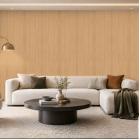 Warm Sand Wood Seamless Wallpaper featuring a subtle natural wood grain texture in soft beige and warm sandy tones, creating a calm, elegant, and sophisticated interior wall finish. The seamless vertical wood pattern adds gentle depth and a natural organic feel while maintaining a clean and refined appearance. The wallpaper is showcased across a spacious feature wall in a bright contemporary living room with neutral cream furniture, a dark round coffee table, textured rug, earthy brown cushion